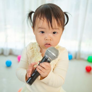 Happy little asian girl with microphone in the home