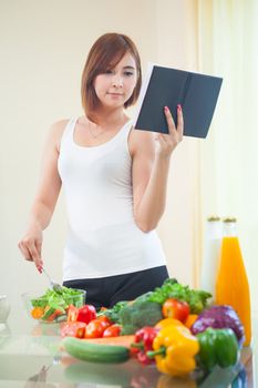 Young asian woman reads cookbook for recipe at kitchen