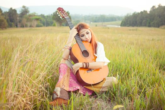 Pretty country hippie girl playing guitar on grass