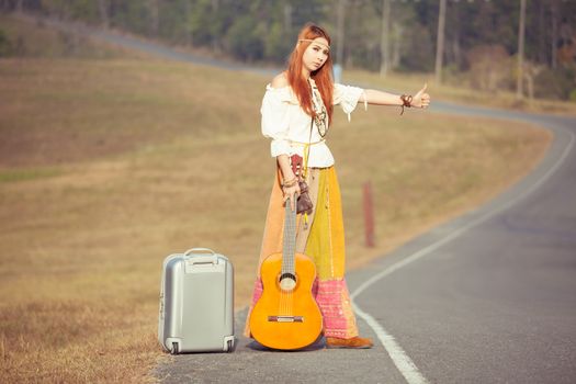 Hippie girl with guitar hitchhiking on countryside road