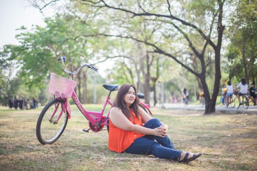 Happy fatty asian woman posing with bicycle outdoor in a park