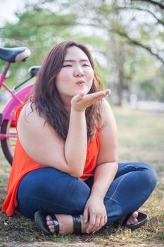 Happy fatty asian woman posing with bicycle outdoor in a park