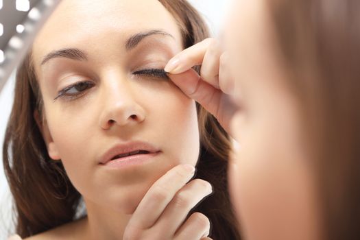 Portrait of a woman that curls lashes standing in front of a mirror