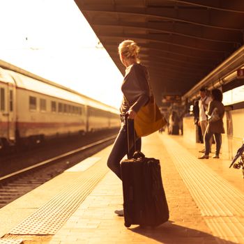 Blonde caucasian woman waiting at the railway station with a suitcase.