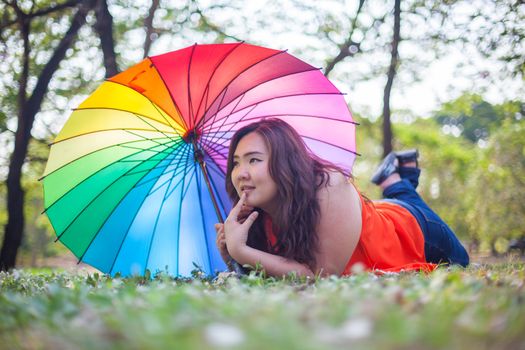 Happy fatty asian woman with umbrella outdoor in a park