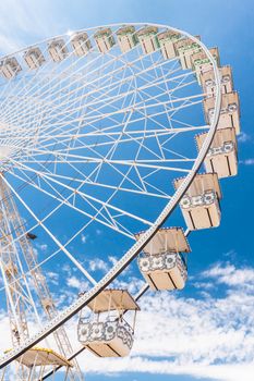 Ferris wheel of fair and amusement park.  White clouds in the blue sky in background.
