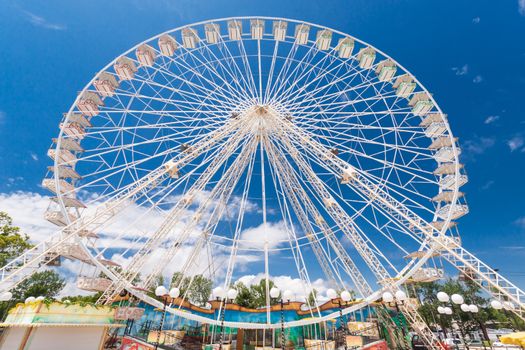 Ferris wheel of fair and amusement park.  White clouds in the blue sky in background.