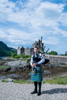 DORNIE, SCOTLAND - June 7, 2014: A bagpipe player with traditional kilt in front of Eilean Donan, the most famous castle in Scotland, on June 7, 2014 in Dornie, Scotland, United Kingdom.