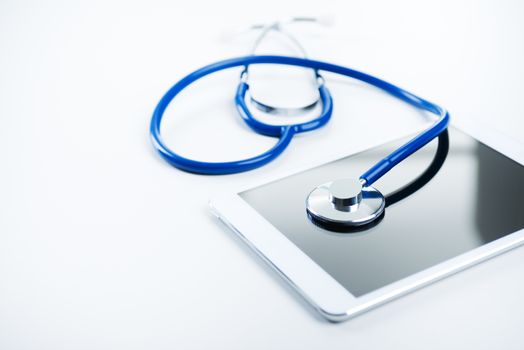 Medical equipment: blue stethoscope and tablet on white background.