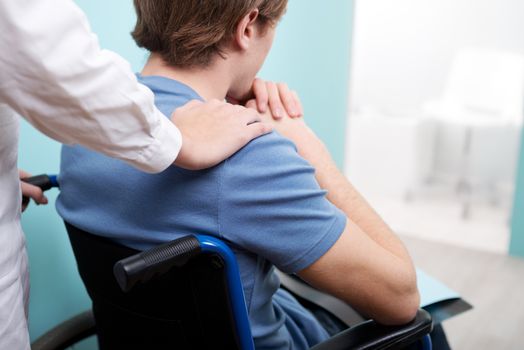 Female doctor consoling young man sitting in wheelchair