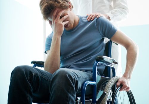 Female doctor consoling sad man sitting in wheelchair