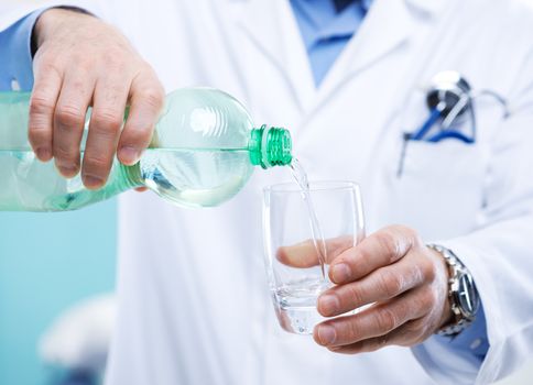 Doctor pouring water out of a bottle into a glass.