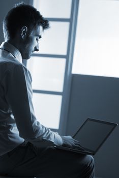 Young man sitting and working with laptop on his lap.