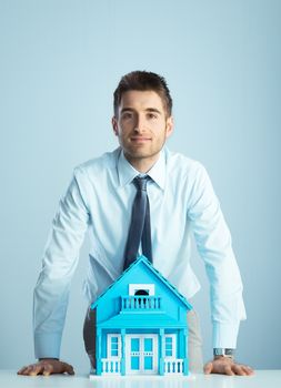 Young real estate agent leaning on desk with model house.