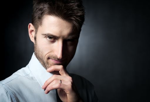 Young confident businessman looking at camera and touching his chin.