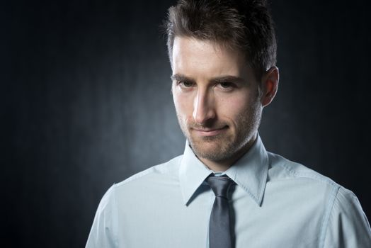 Attractive young businessman looking at camera and smiling on dark background.
