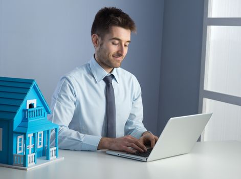 Man working with laptop at his desk and model house.