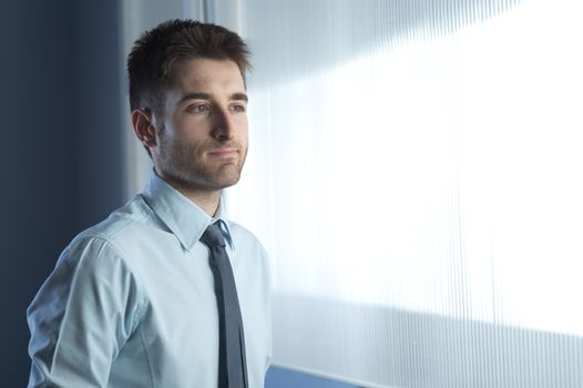 Young businessman at window looking away and thinking.