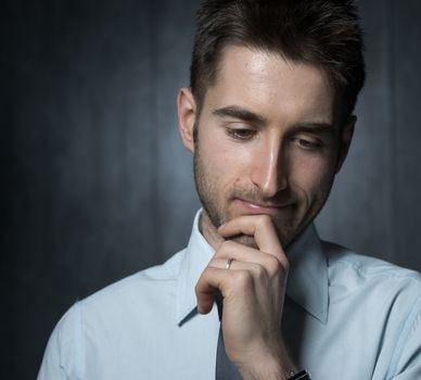 Young handsome businessman thinking with hand on chin.