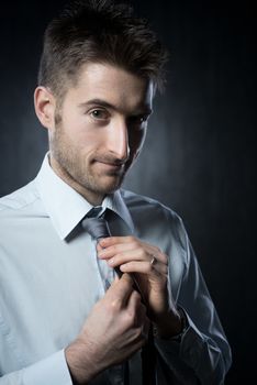 Young elegant man adjusting tie knot and smiling.