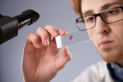 Chemical laboratory technician holding a microscope slide with blood sample.