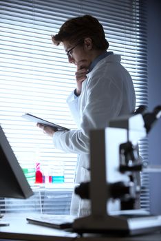 Researcher reading medical records in the chemical laboratory with microscope on foreground.