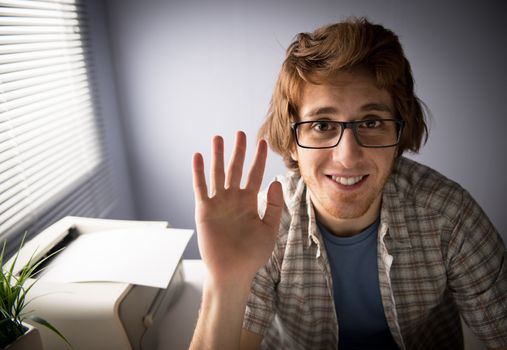 Young man video calling and waving hand with funny expression.