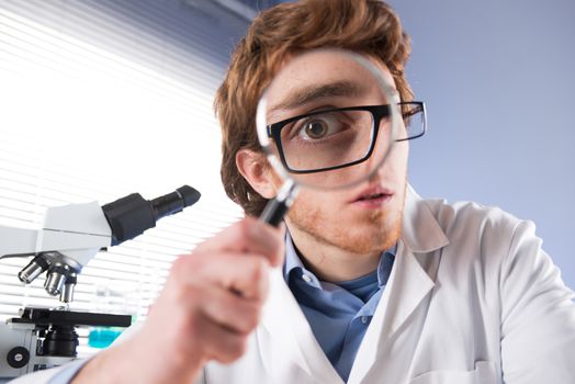 Young researcher looking through magnifier with surprised expression.