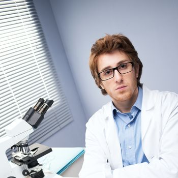 Student researcher at desk with microscope on background.
