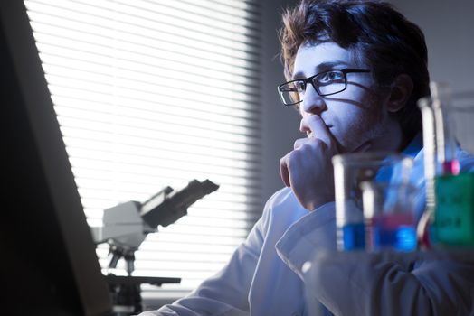 Researcher working at computer in the laboratory with hand on chin.