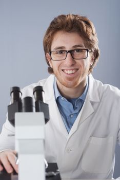 Student researcher using microscope and smiling at camera.
