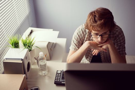 Young bored guy at office staring at computer screen.