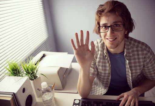 Young friendly guy smiling on web cam and waving hand.