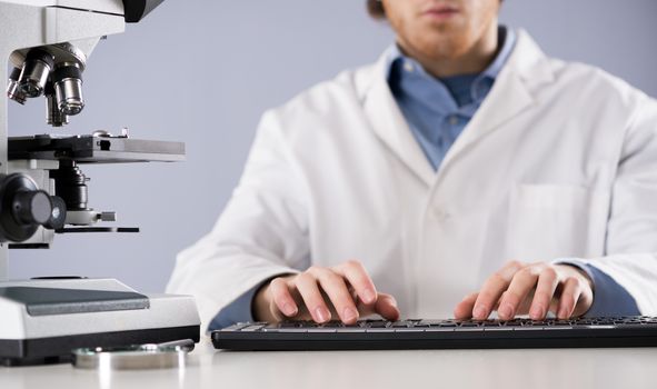 Researcher working at desk and typing on a keyboard, with microscope and magnifier.