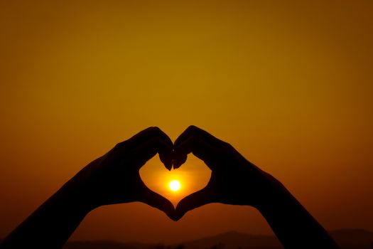 Silhouettes hand heart shaped  with sun sets and the sky orange