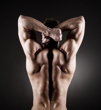 Body builder posing on dark background, rear view.