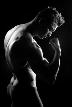 Body builder posing and showing off bicep muscle on dark background.