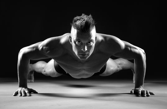 Muscular man doing push-ups  and looking forward on dark background.