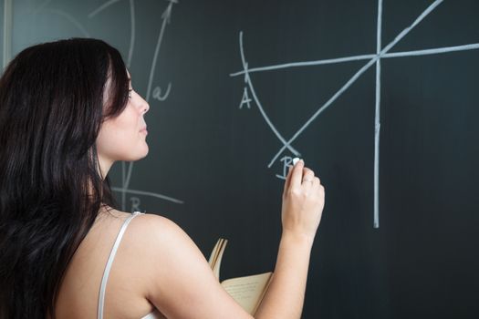 Pretty, young college student drawing on the chalkboard/blackboard during a math class (shallow DOF; color toned image)