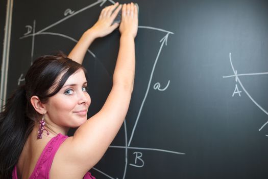 Pretty, young college student drawing on the chalkboard/blackboard during a math class (shallow DOF; color toned image)