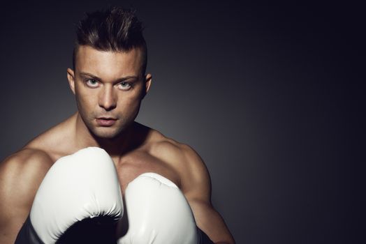 Boxer posing on dark background with fists raised.