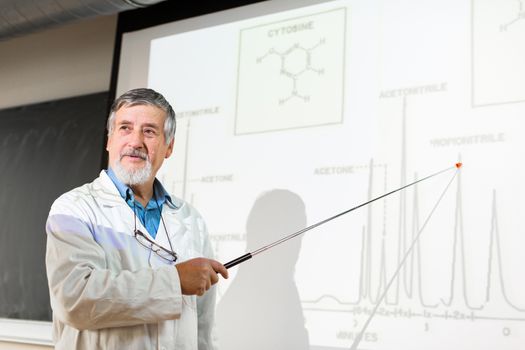 Senior chemistry professor giving a lecture in front of classroom full of students (shallow DOF; color toned image)