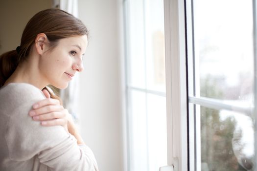 Woman lookong from a window of her house on a cold and snowy winter day