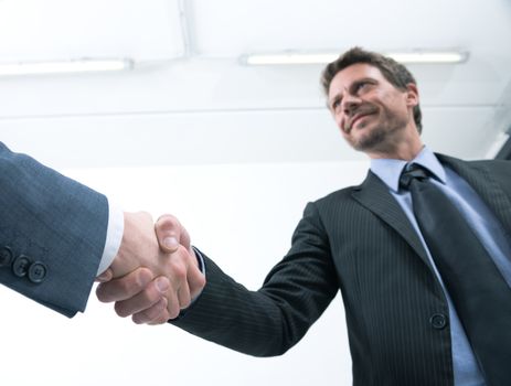 Confident businessmen shaking hands with empty white room on background.