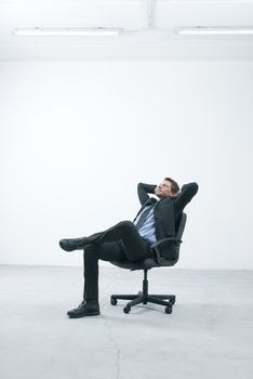 Thinkful businessman sitting on office chair with hands behind head in his new empty office.