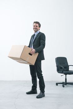 Smiling businessman holding a cardboard box and standing in an empty new office.