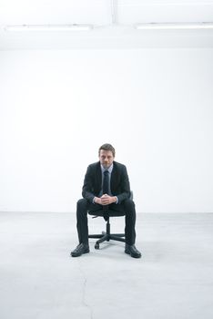 Elegant businessman sitting on an office chair in an empty room looking at camera.
