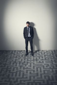 Pensive businessman looking at maze on the floor leaning to a wall.