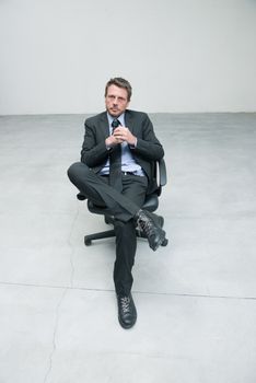 Businessman sitting on an office chair against concrete floor background.