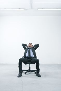 Thinkful businessman sitting on office chair with hands behind head in his new empty office.